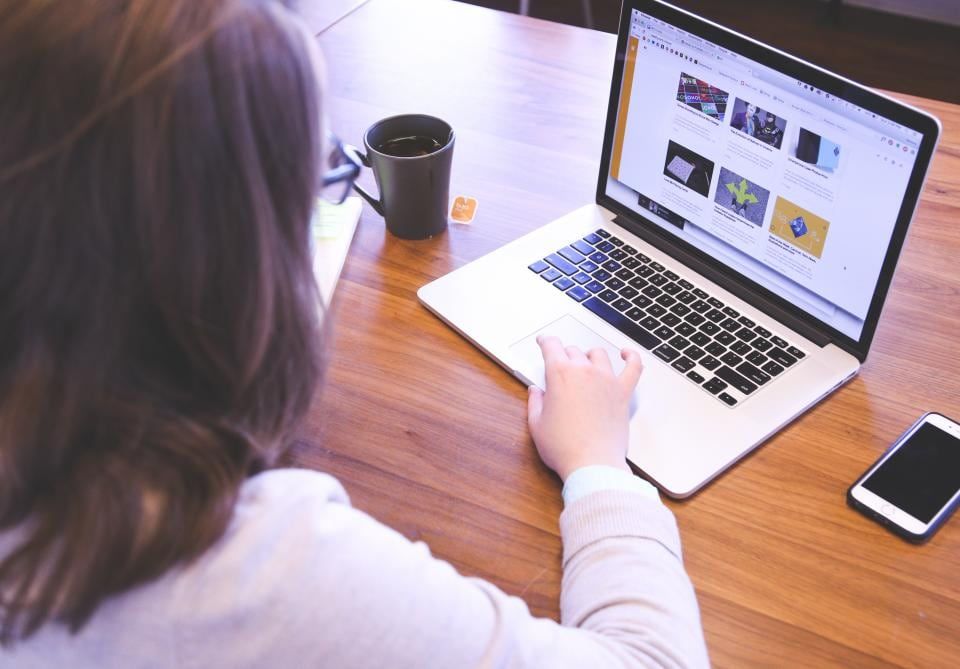 A woman working through emails on a laptop at a wooden desk with a mug and phone beside her